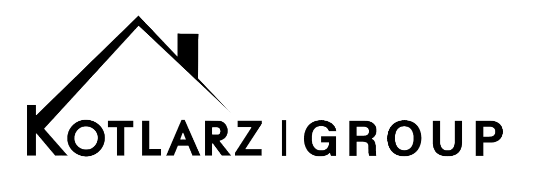 The Kotlarz Group logo features a clean and modern black-and-white design. The "K" in "Kotlarz" is integrated into a stylized house roofline, which extends diagonally upward, forming a triangular peak. A small chimney is positioned on the right side of the roof, reinforcing the real estate or housing-related theme. The text "Kotlarz Group" is written in a bold, sans-serif font, separated by a vertical bar. The use of black and white adds a sleek and professional appearance, making the logo visually strong and easy to recognize.